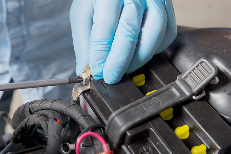 man in blue gloves using a screwdriver to replace battery in a motorcyle after cleaning terminals