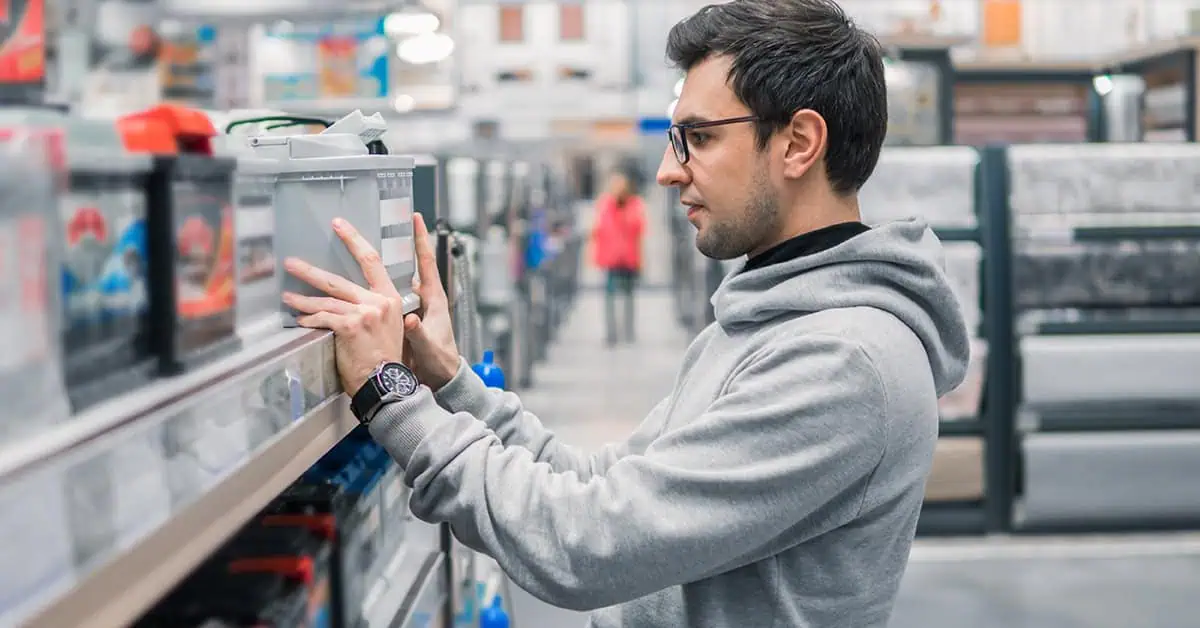 Man learning how to read yuasa battery names, holding a battery in a store.