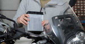Woman holds a motorcycle battery while performing seasonal maintenance.