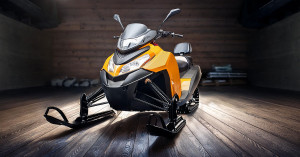 A yellow snowmobile sits in an open wooden garage.