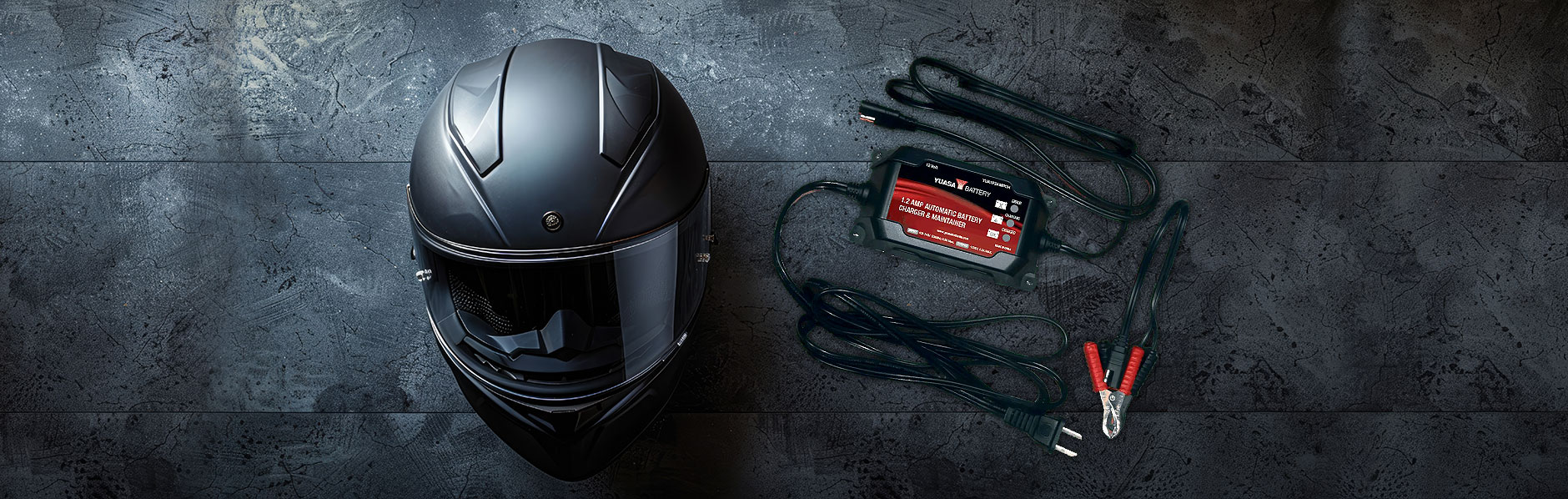 Motorcycle helmet besides a battery maintainer on a grey granite background.