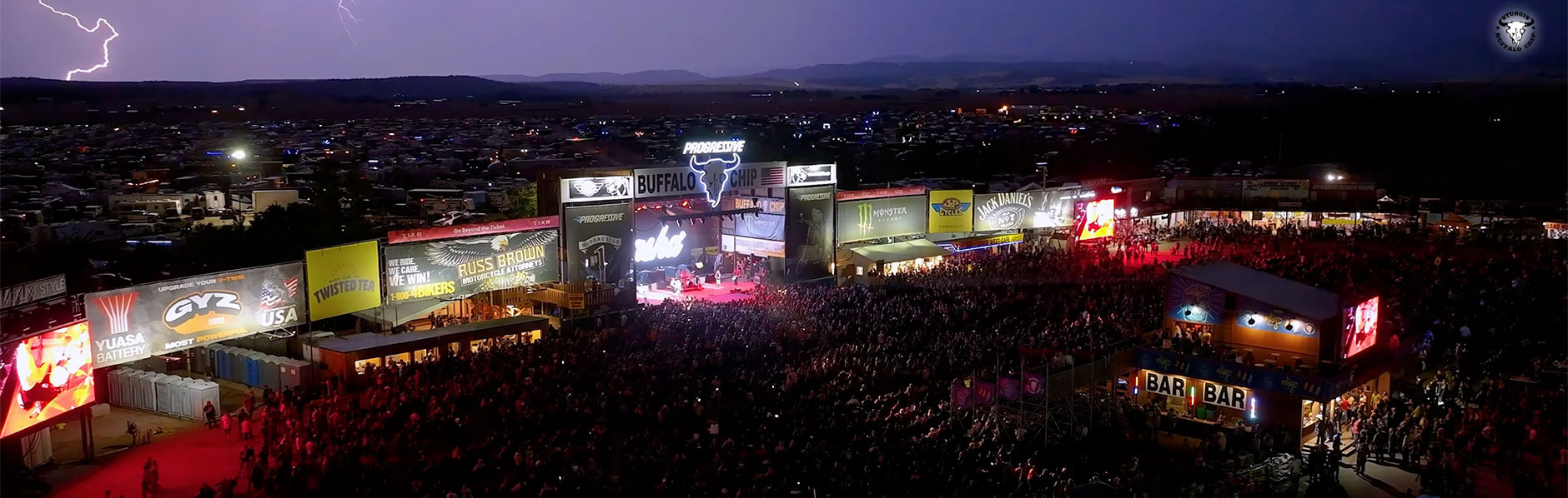 Buffalo Chip Garage stage surrounded by concertgoers and background with lightning in the sky.